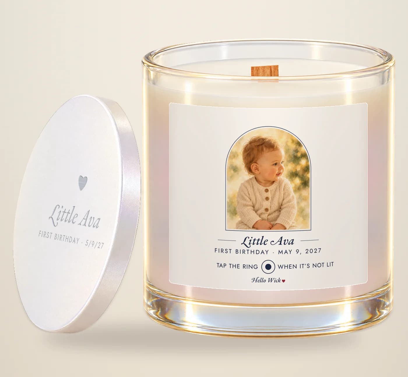 A Hello Wick candle labelled Little Ava, first birthday, with a watercolour of the baby in the arch and its engraved lid beside it