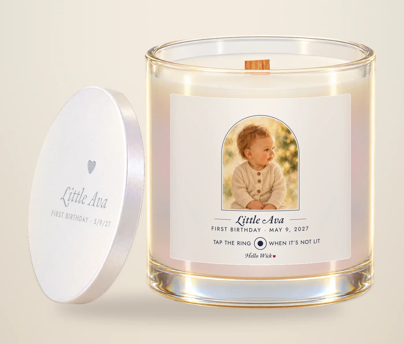 A Hello Wick candle labelled Little Ava, first birthday, with a watercolour of the baby in the arch and its engraved lid beside it