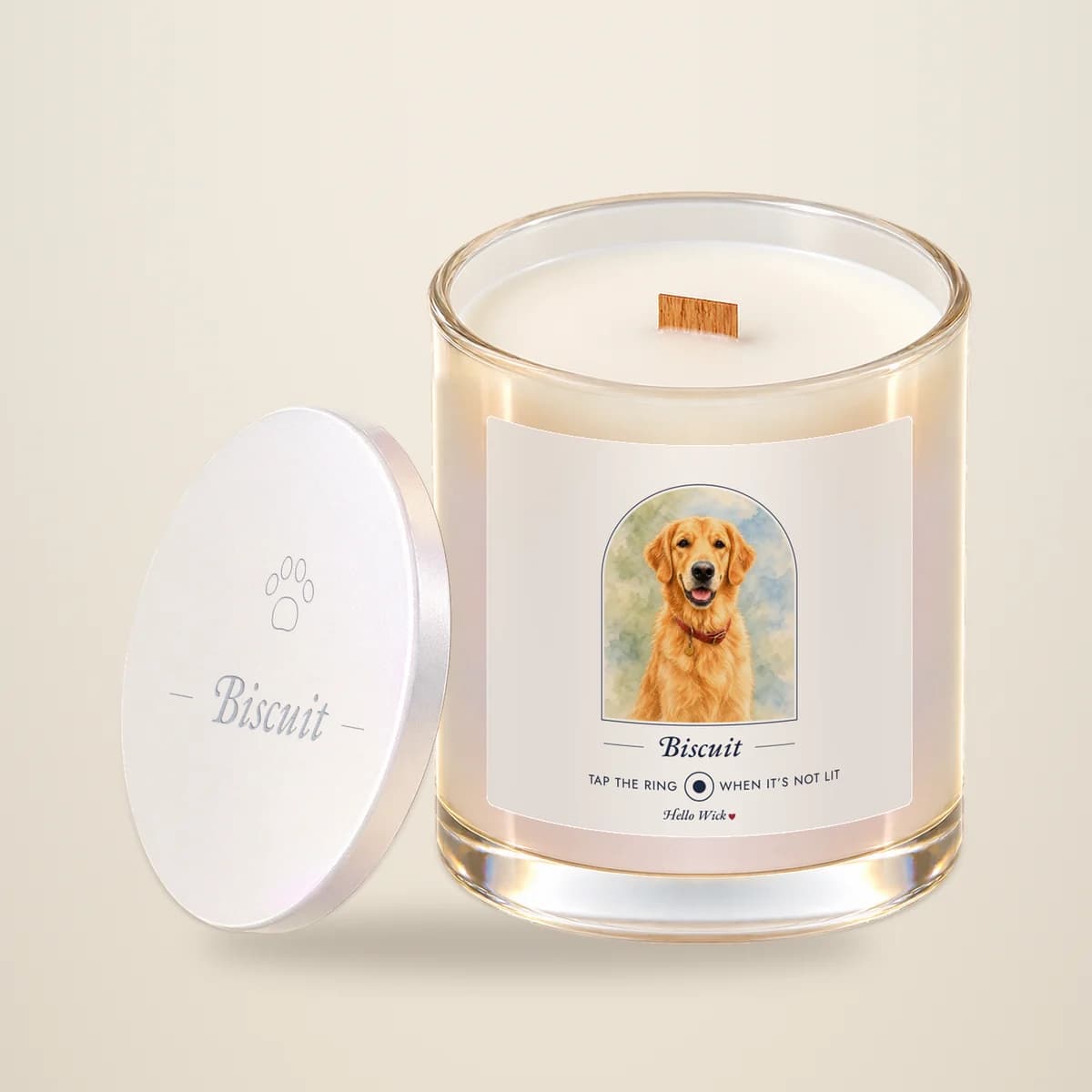 A Hello Wick candle labeled Biscuit, with a watercolor of the dog in an arch, its lid leaning beside it