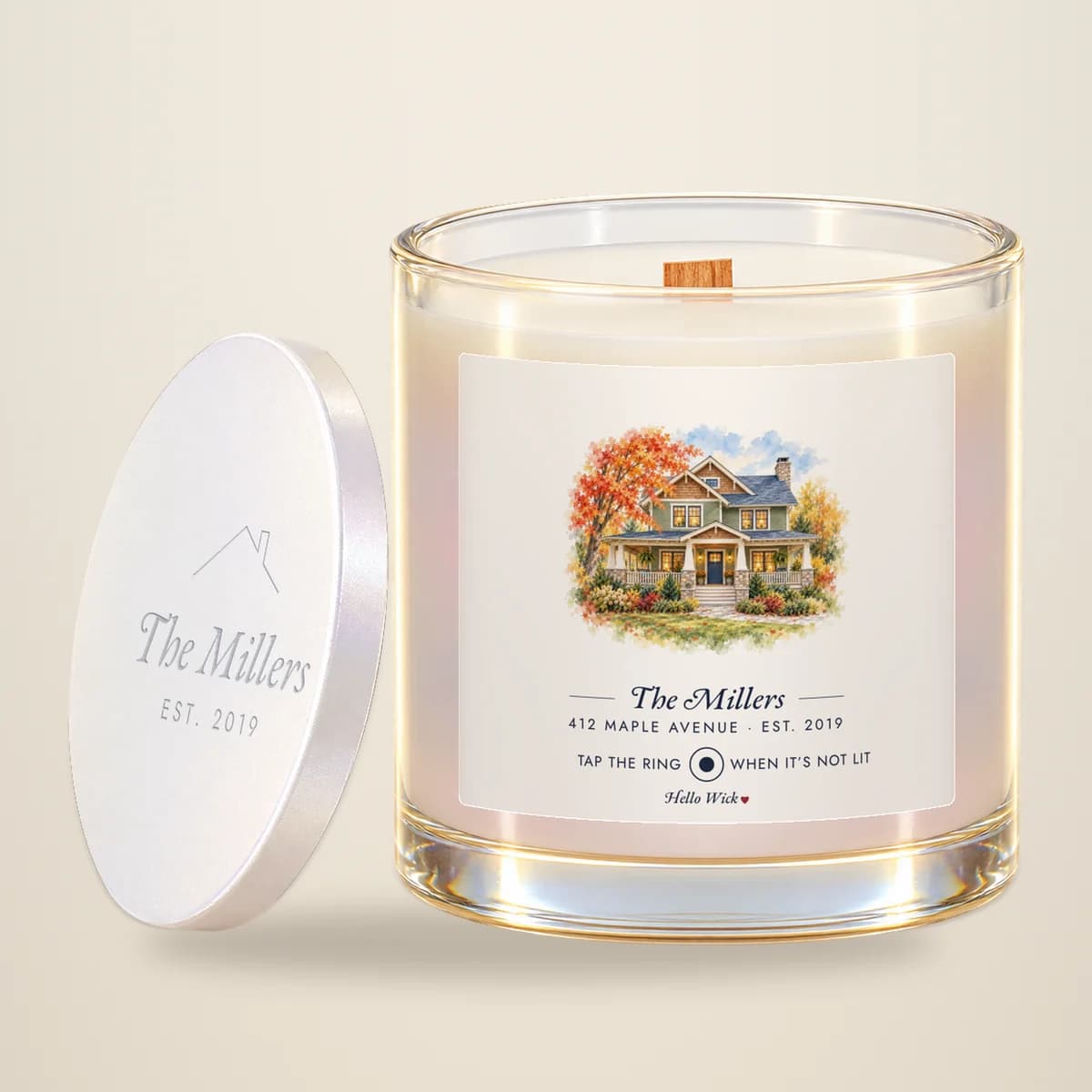 A Hello Wick candle labeled The Millers, with a watercolor of their house, its lid leaning beside it
