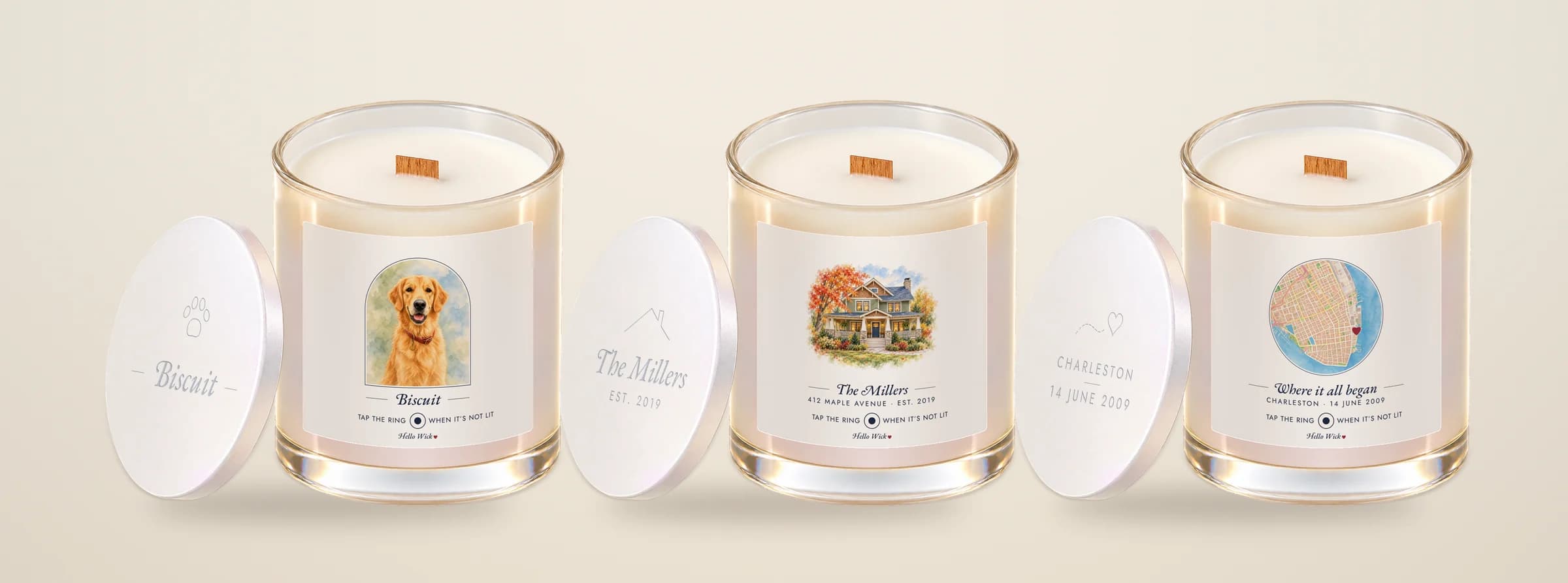 Three Hello Wick candles with their lids leaning beside them: Biscuit with a watercolor dog in an arch, The Millers with a watercolor house, and Where it all began with a round watercolor map of Charleston